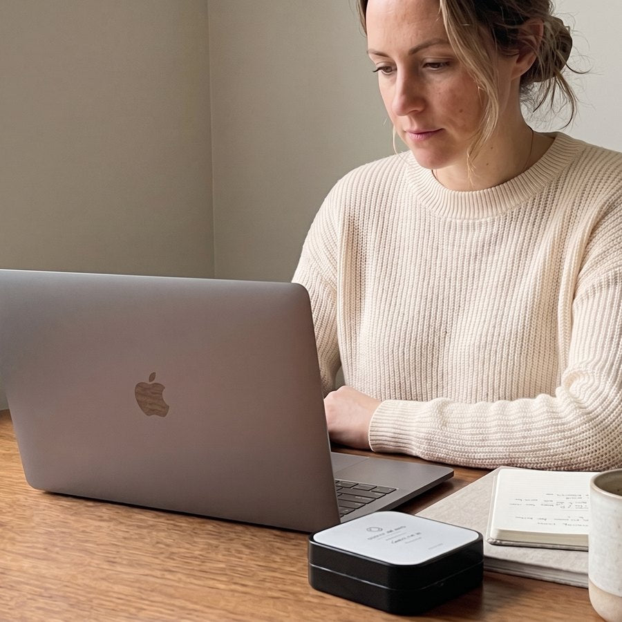 An agency owner working at a laptop at a wooden table, an Axiom Focus tin beside her notebook and coffee.