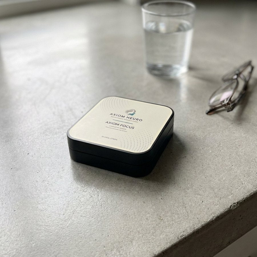 An Axiom Focus tin on a kitchen counter beside a glass of water and reading glasses.